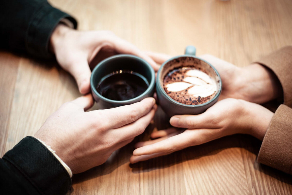 wo person holding ceramic mugs with coffee on first date
